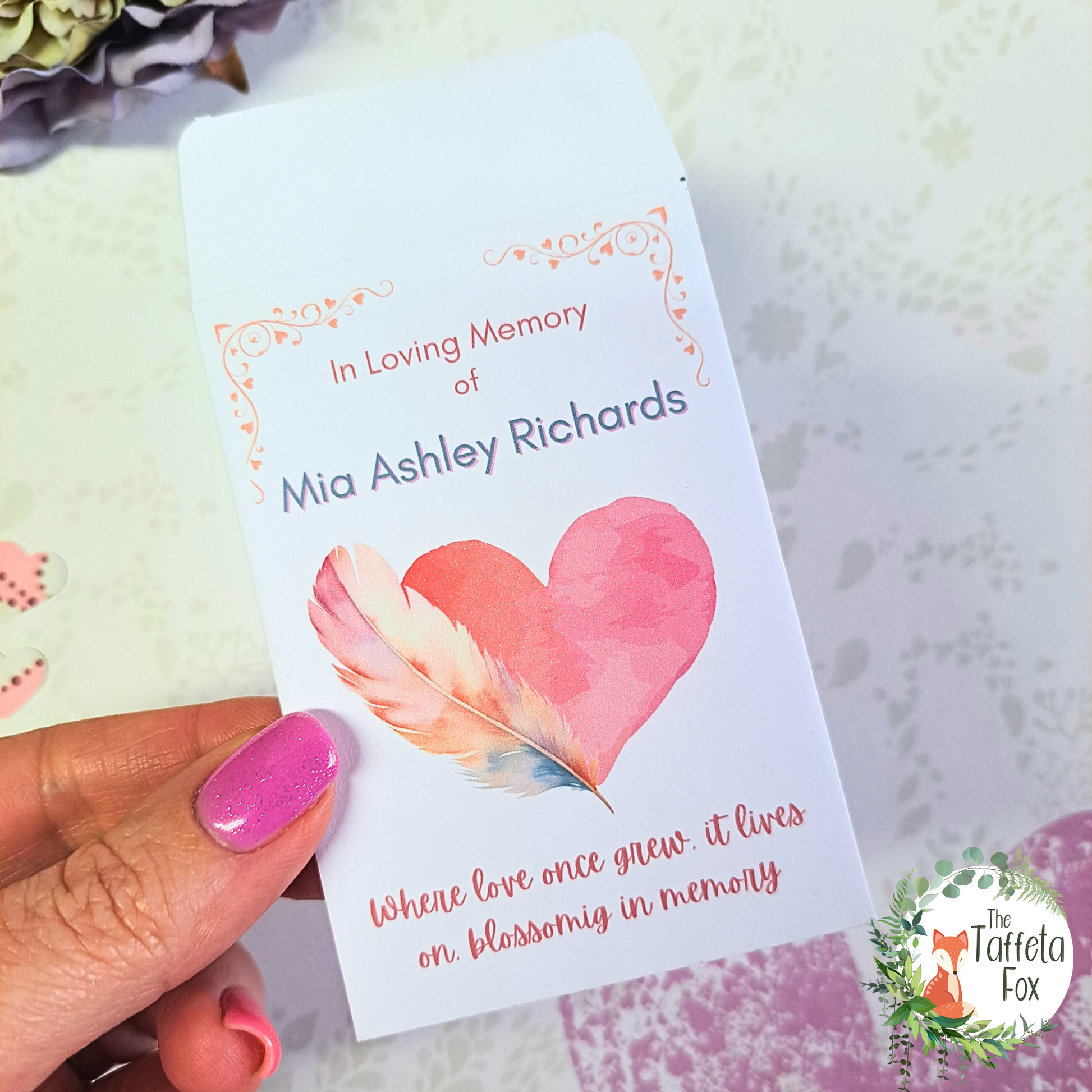 In Loving Memory personalised seed packet featuring a pink heart and feather illustration, designed as a funeral or celebration of life favour.