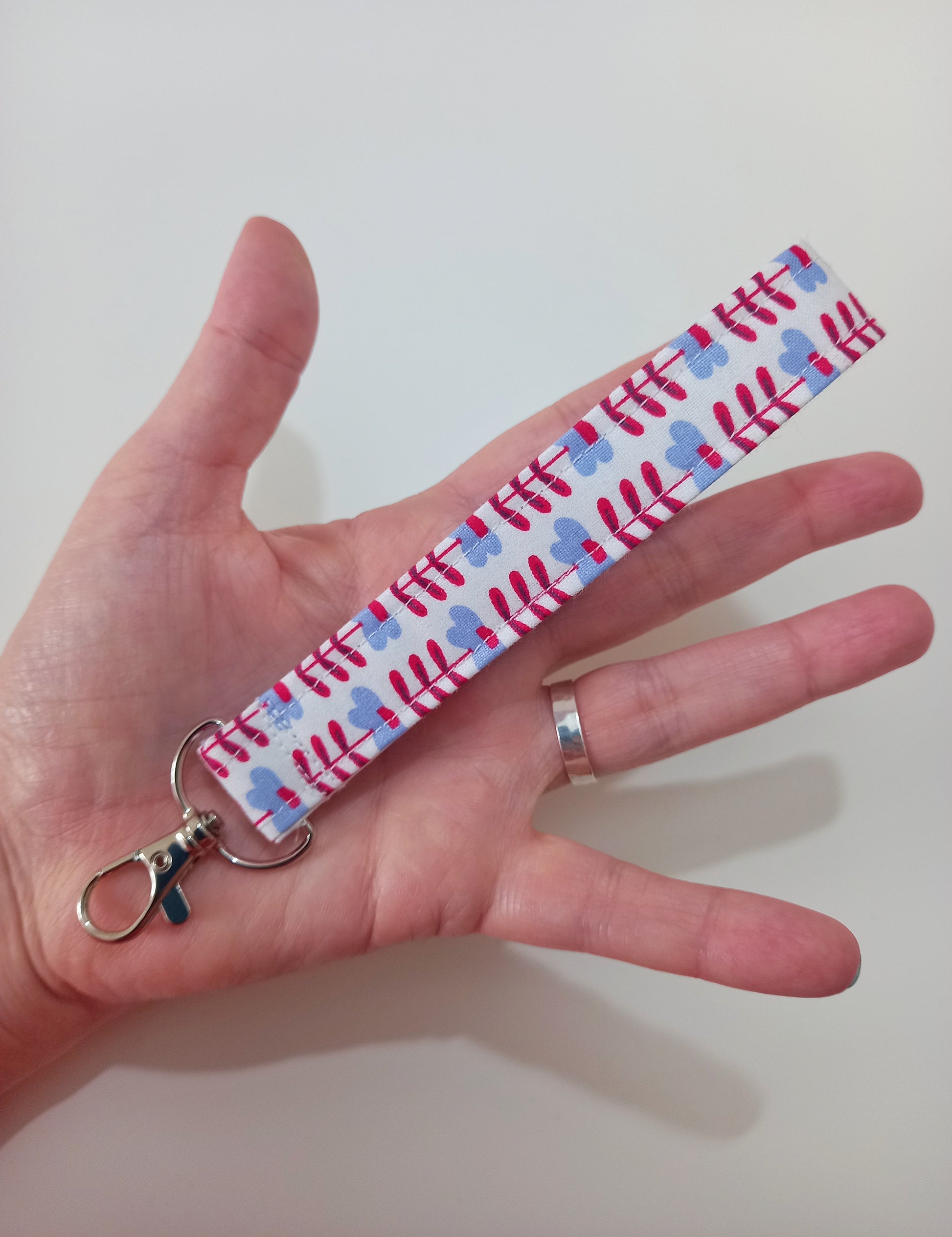 Our fabric wristlet in a white fabric with retro floral pattern with sewn in silver keyfob.  It's resting on the palm of an open hand to show size.