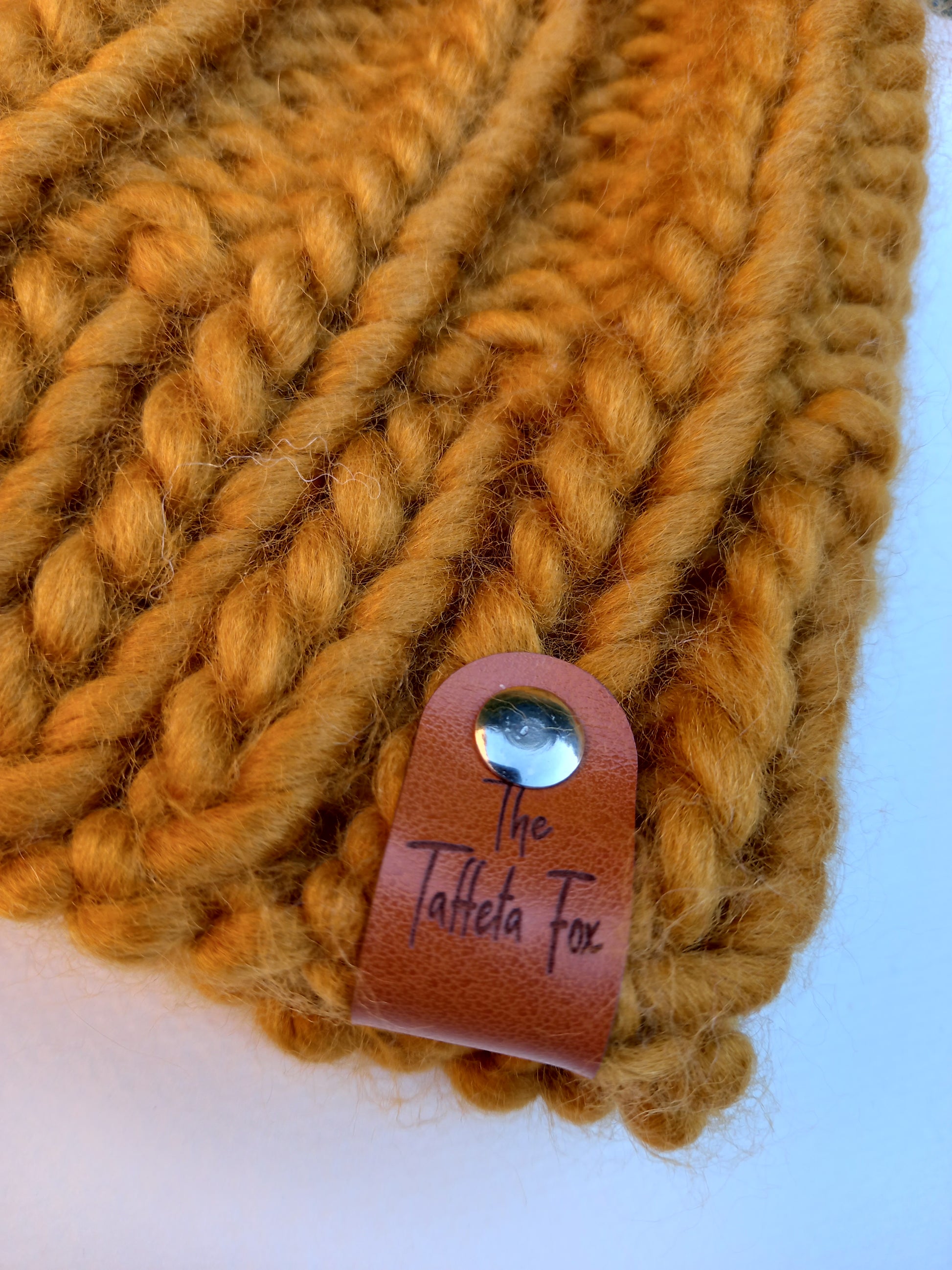 This image shows a close up of the brown faux leather The Taffeta Fox label attached to the brim of the hat with a small silver rivet. 