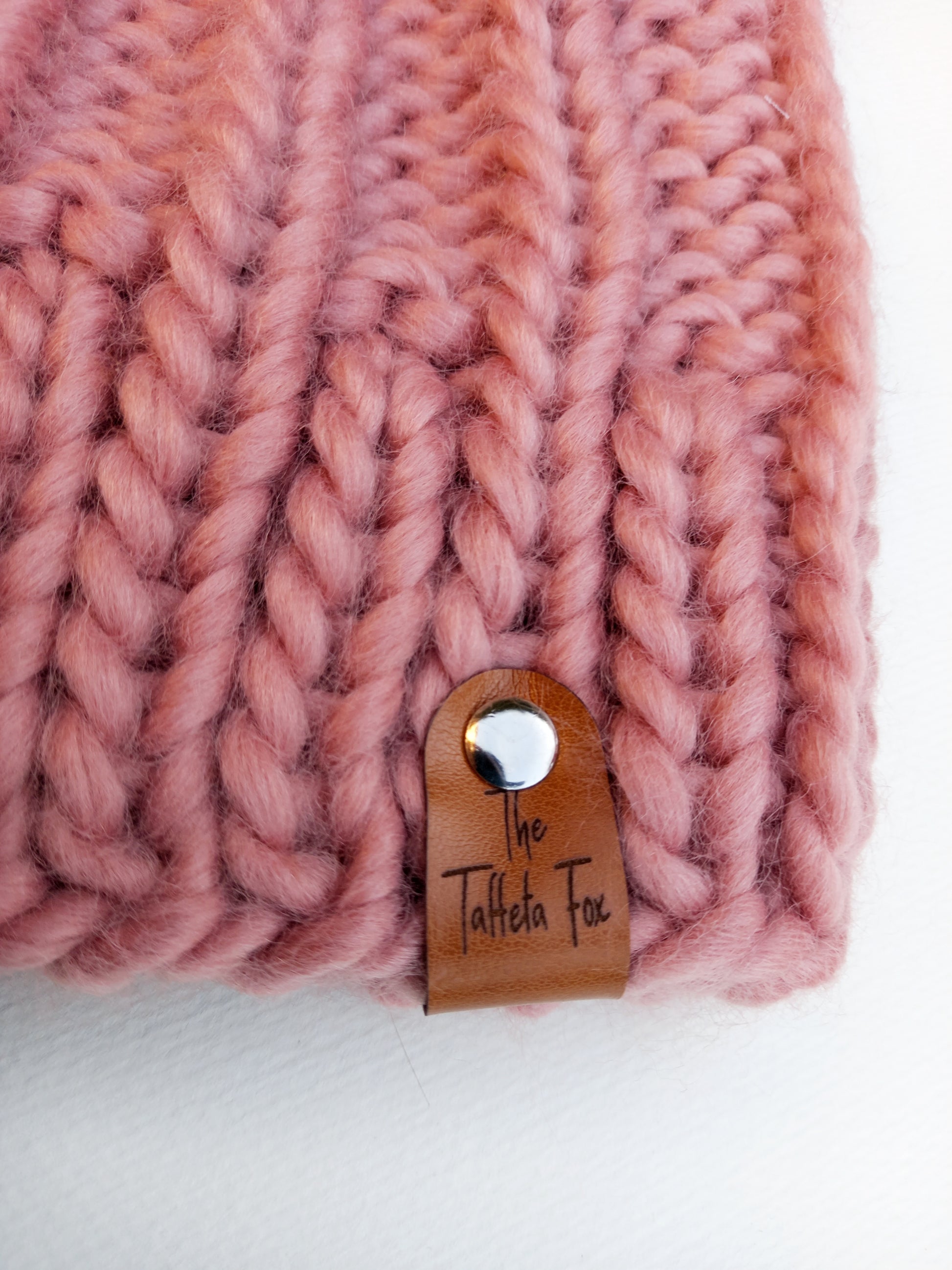 This image shows a close up of the brown faux leather The Taffeta Fox label attached to the brim of the hat with a small silver rivet. 