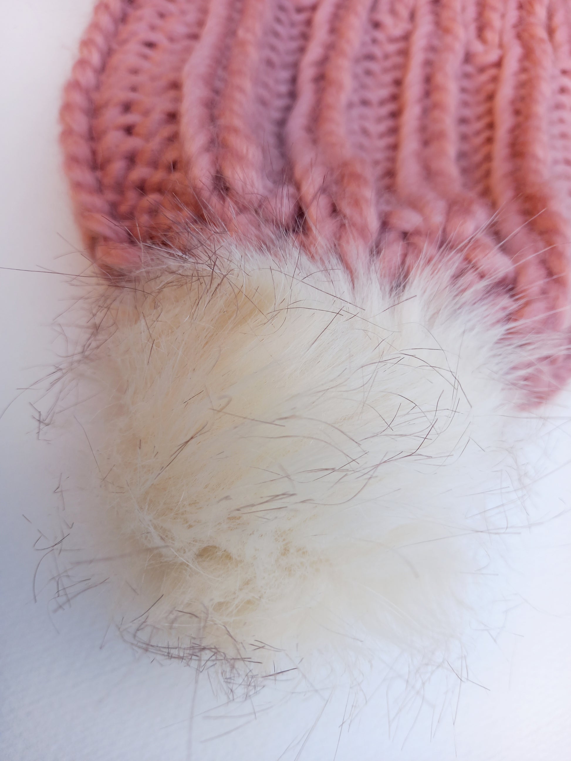 This is a close up of the off-white pompom attached to the handknitted super chunky pink hat. 