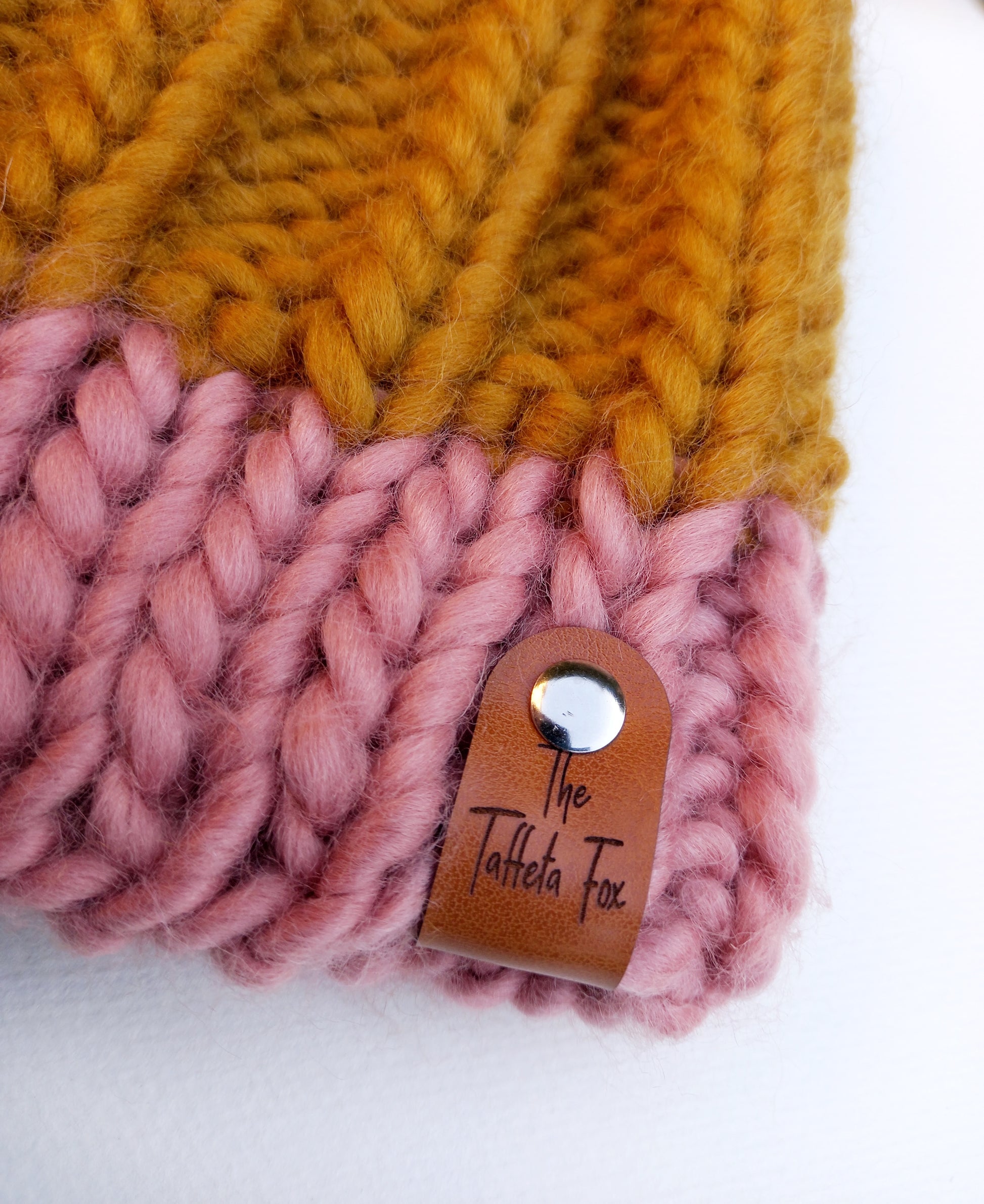 This image shows a close up of the brown faux leather The Taffeta Fox label attached to the brim of the hat with a small silver rivet. 