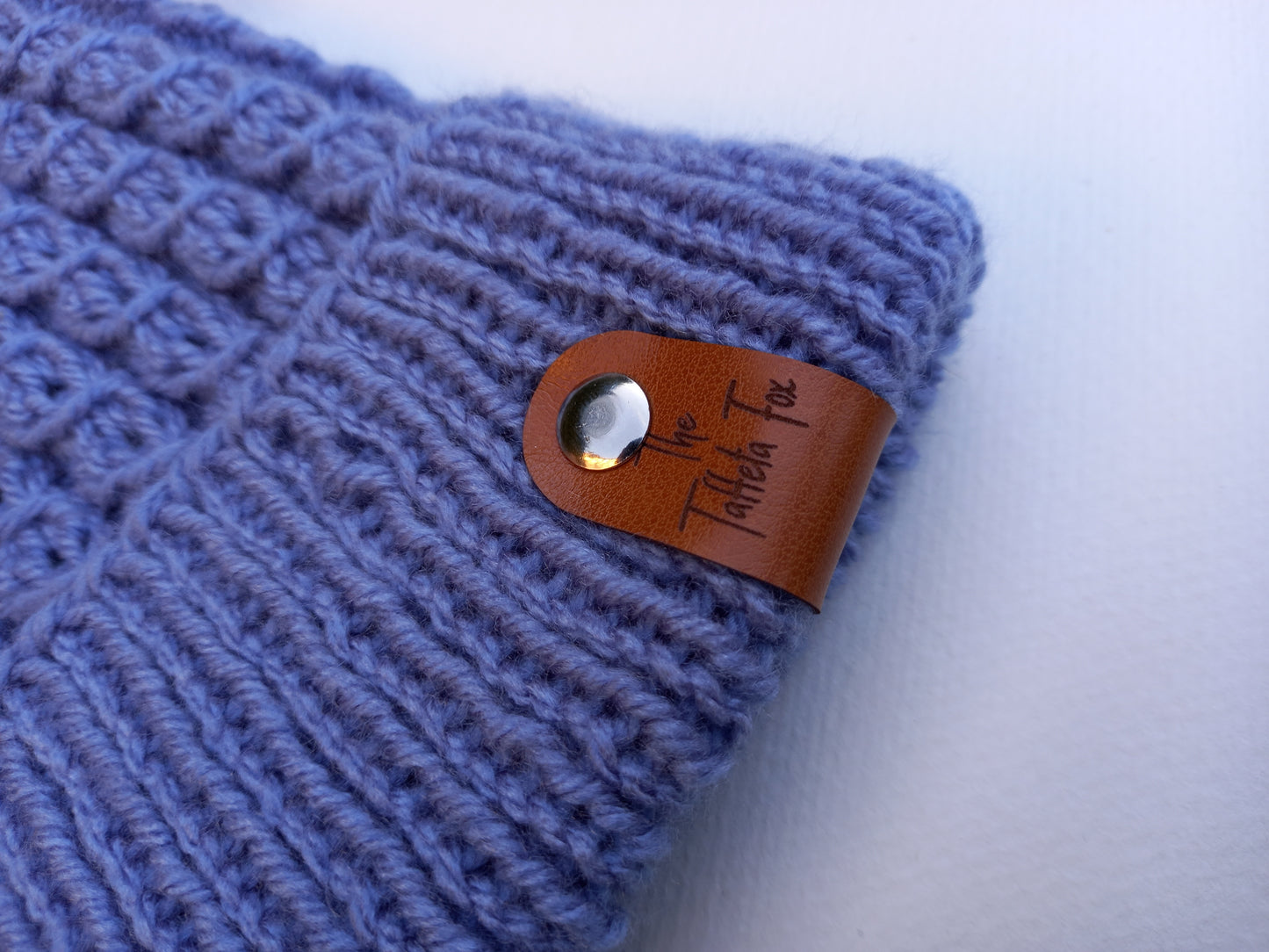 A close up of the brown faux leather The Taffeta Fox tag attached via a silver rivet.