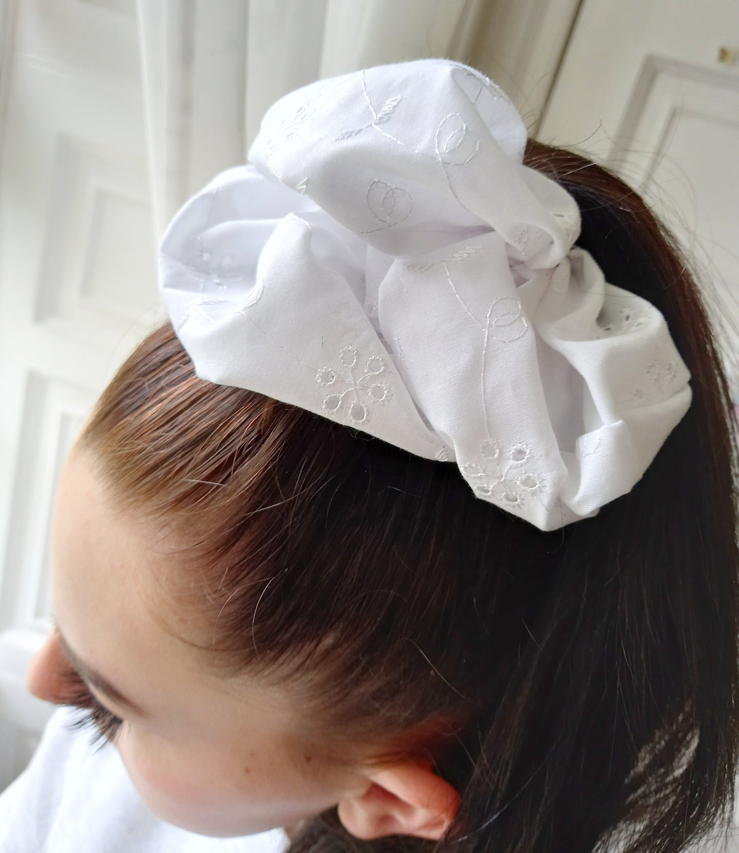 White broiderie anglaise XL oversized scrunchie worn in the hair of a young woman with long dark hair.